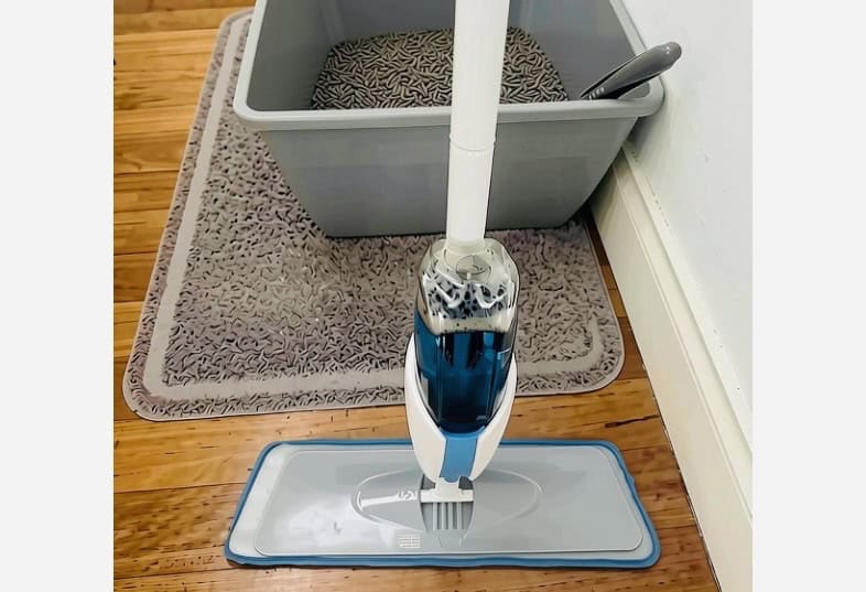 grey cat litter box on mat on wooden floor with spray mop resting on it